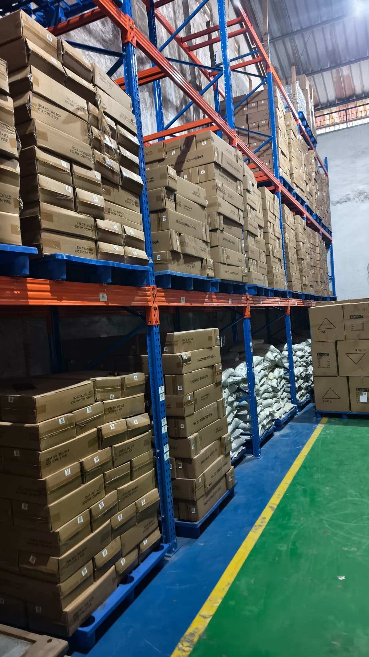 Lorong gudang Indonesia dengan karton APAR dan karung dry powder